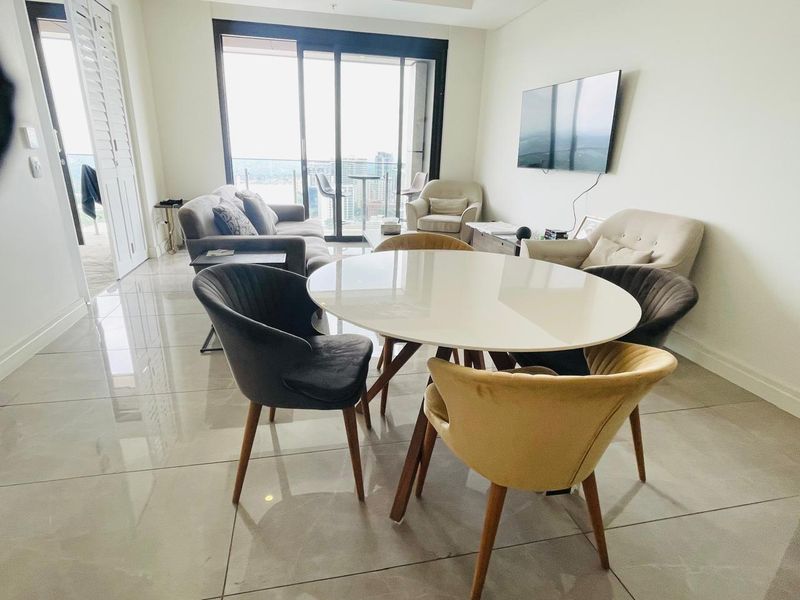 Bright open-plan living and dining area featuring large format floor tiles, recessed ceiling details, and expansive sliding glass doors leading to a balcony.