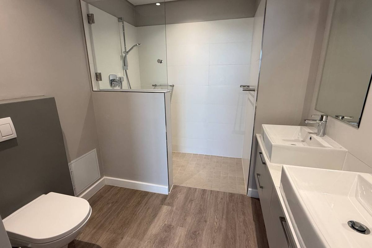 Modern bathroom featuring a spacious walk-in shower with glass screen, dual vanity basins, and a wall-hung toilet with contemporary finishes.