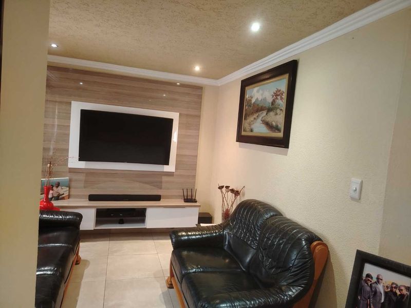 A comfortable living room featuring a modern built-in media unit, recessed downlighting, and neutral tiled flooring.