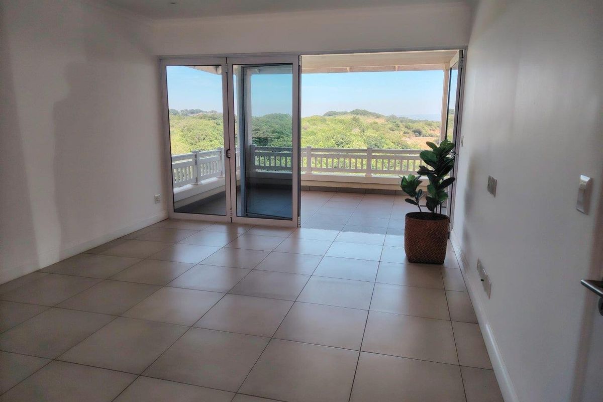 Bright and spacious living area featuring neutral tiled flooring and large sliding glass doors that open onto a balcony with scenic views.