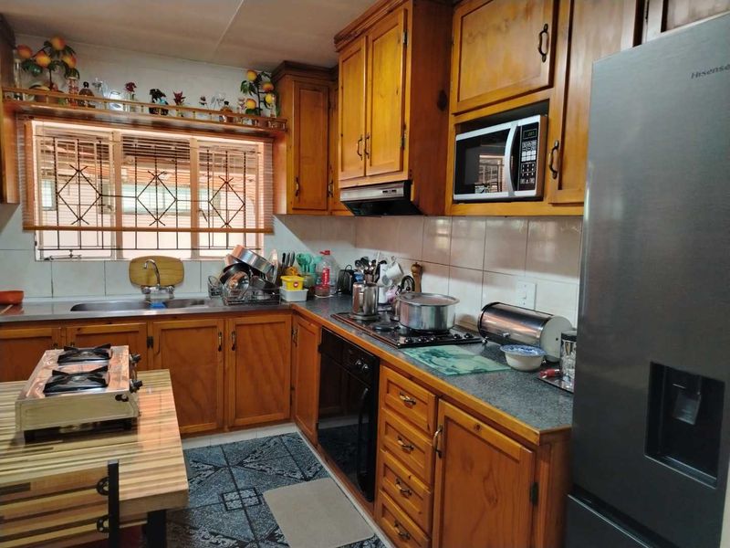 A functional kitchen featuring traditional wooden cabinetry, built-in appliances, a gas hob, and a tiled backsplash with security bars on the window.