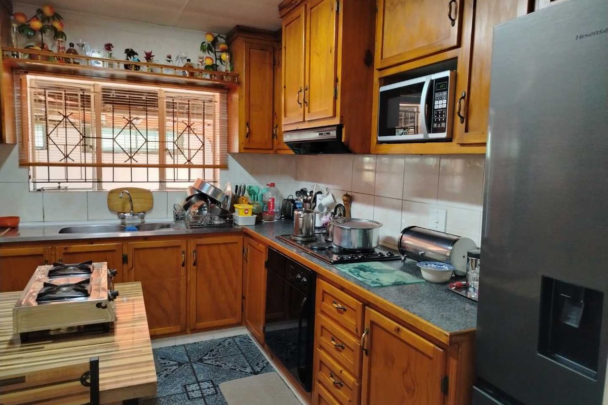 A functional kitchen featuring traditional wooden cabinetry, built-in appliances, a gas hob, and a tiled backsplash with security bars on the window.