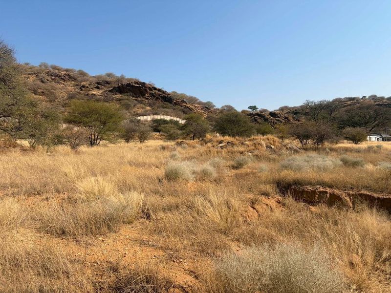 A view of the vacant commercial land featuring natural rocky terrain, indigenous vegetation, and open landscape under a clear sky.