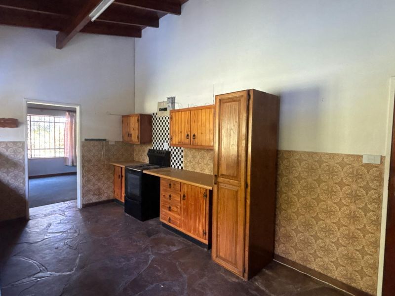 A spacious kitchen featuring exposed timber ceiling beams, stone flooring, wooden cabinetry, and a freestanding stove, offering significant potential for modernization.