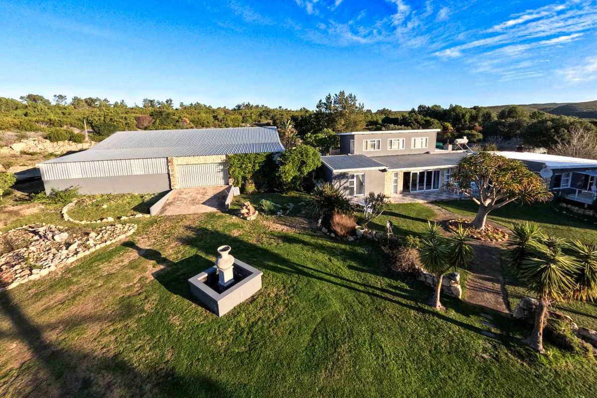 Aerial view of the farm property featuring a main residence, a large metal-clad outbuilding, landscaped garden areas, and a paved patio space.