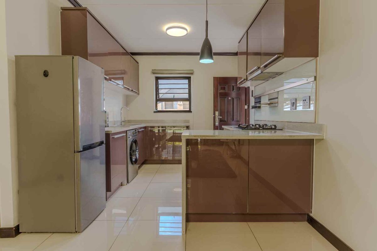 Modern kitchen featuring high-gloss cabinetry, stone countertops, a built-in gas hob, and a mirrored splashback, offering a sleek and functional cooking space.