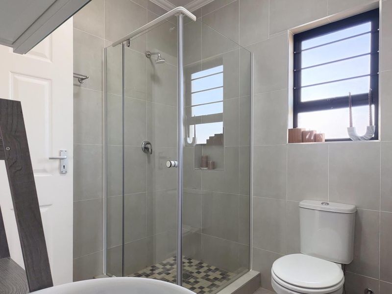 Modern bathroom featuring a glass-enclosed shower with tiled walls, a recessed shelf, and a standard toilet.