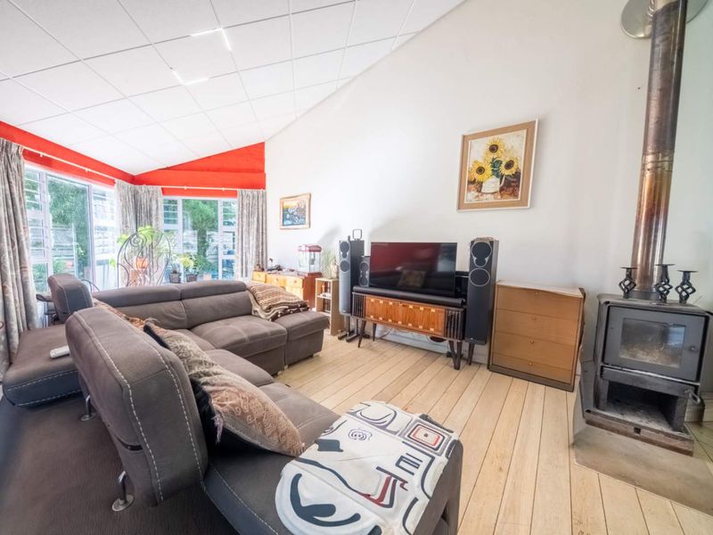 Spacious living room featuring a wood-burning fireplace, timber flooring, and a high raked ceiling with large sliding doors leading to the garden.