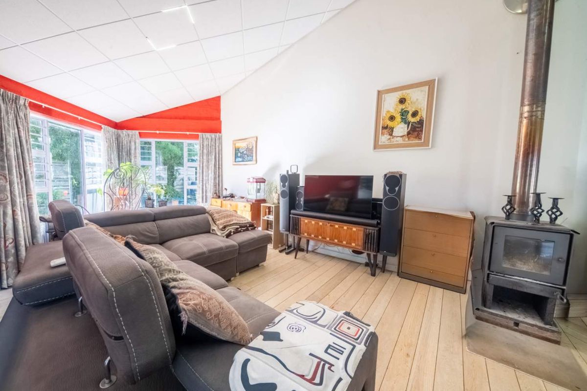 Spacious living room featuring a wood-burning fireplace, timber flooring, and a high raked ceiling with large sliding doors leading to the garden.