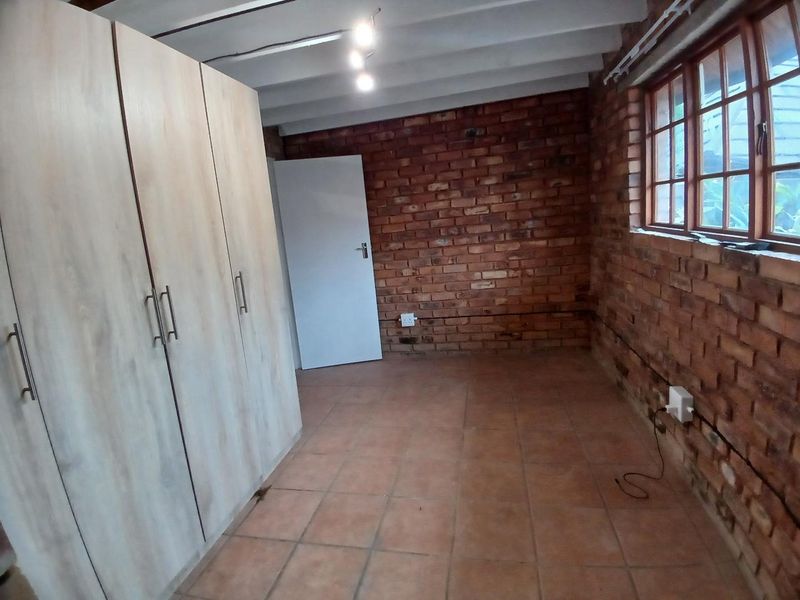 A bedroom featuring exposed brick walls, timber frame windows, tiled flooring, and a built-in wardrobe under an exposed beam ceiling.