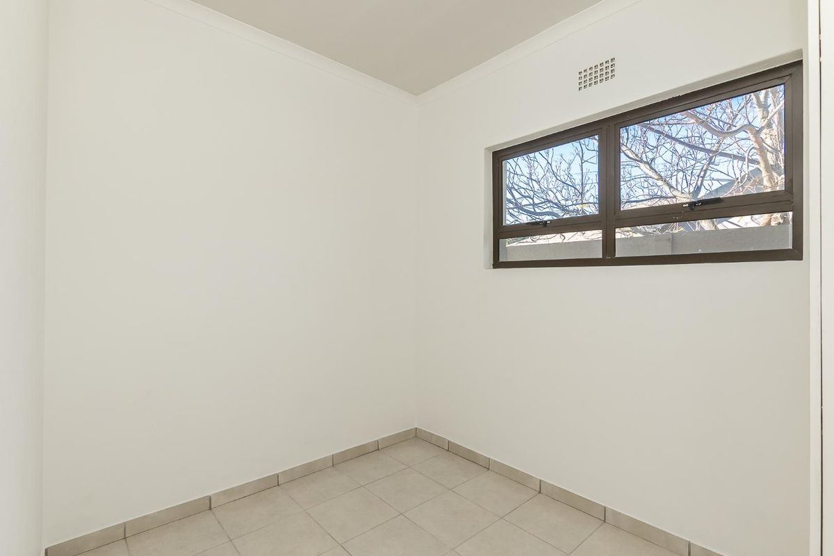 A clean, empty bedroom featuring neutral tiled flooring, white walls, and an aluminium-framed window with an integrated air vent.