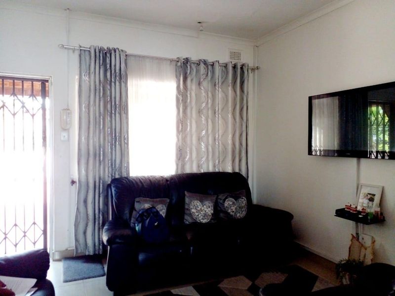 A living room featuring a security gate entrance, curtained window, and wall-mounted television.