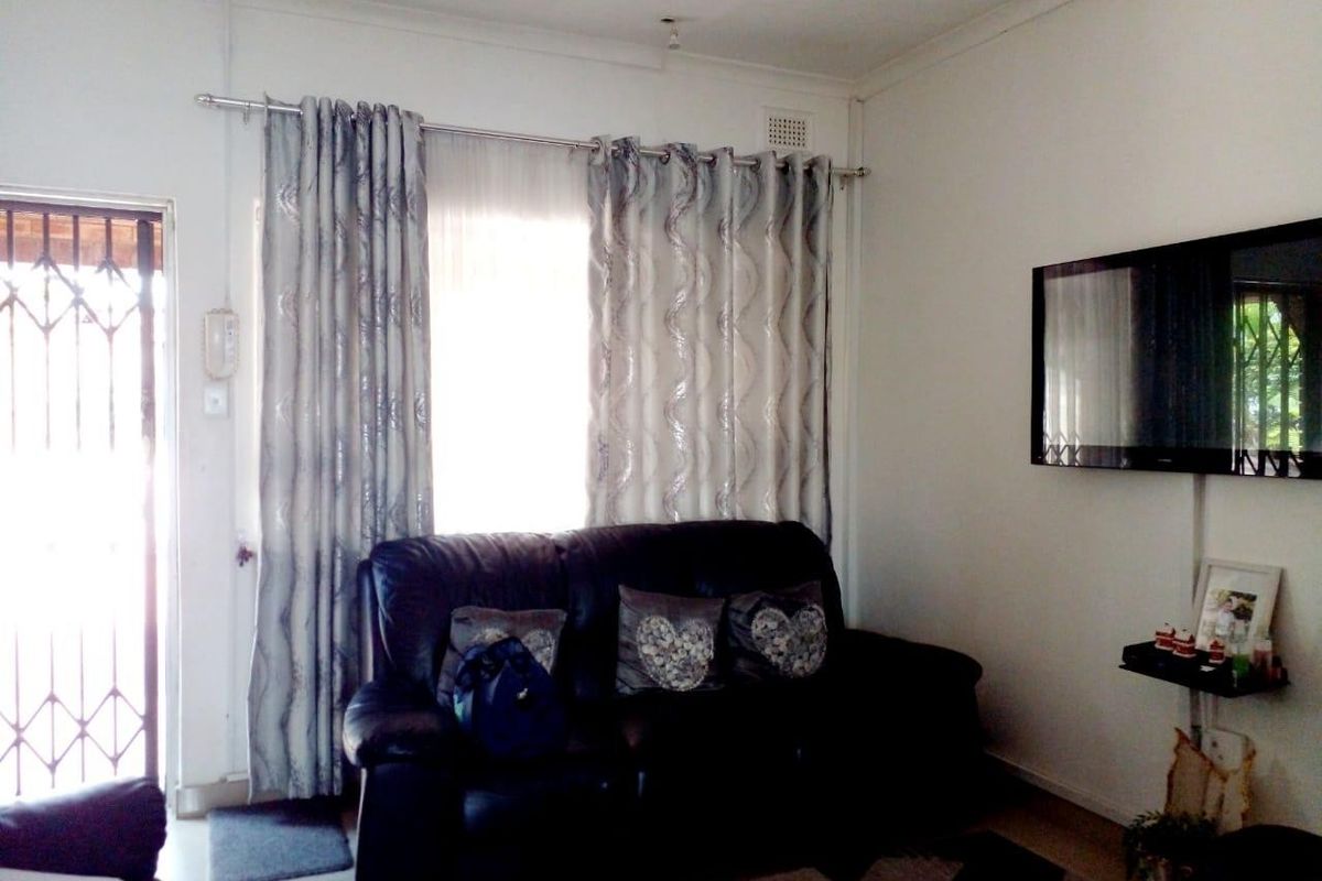 A living room featuring a security gate entrance, curtained window, and wall-mounted television.