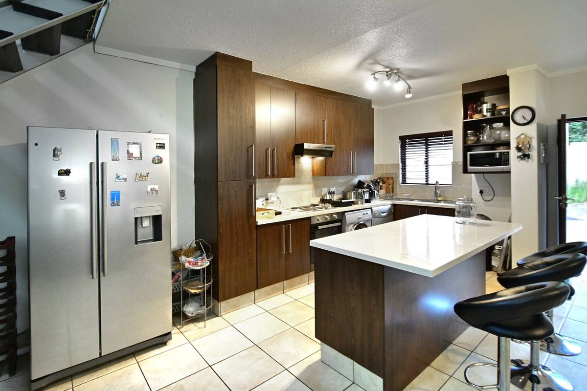 A functional kitchen featuring dark wood cabinetry, a central island with a stone countertop, tiled flooring, and integrated appliances.