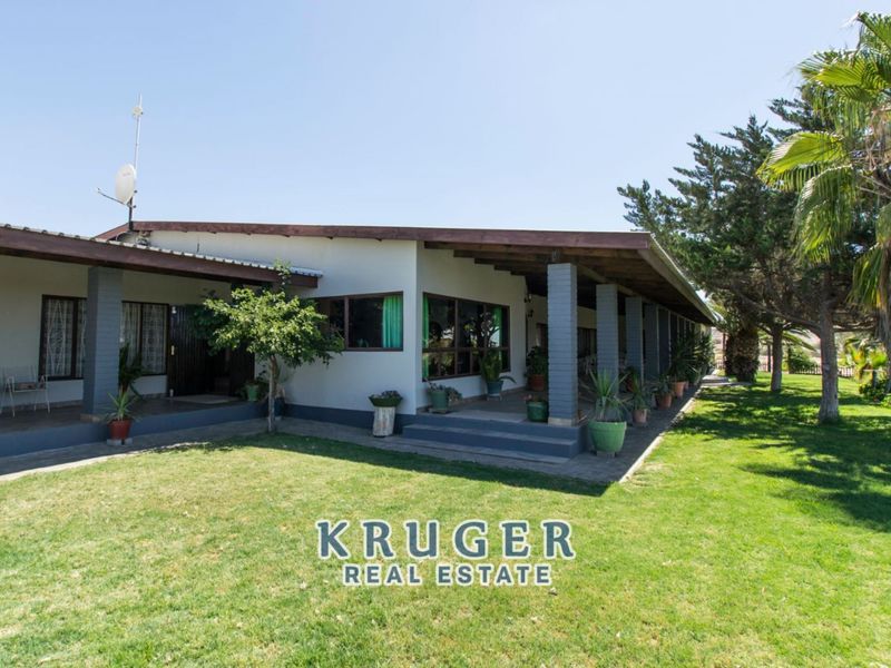 A spacious exterior view of the property featuring a large covered patio area with brick pillars, overlooking a well-maintained garden lawn.