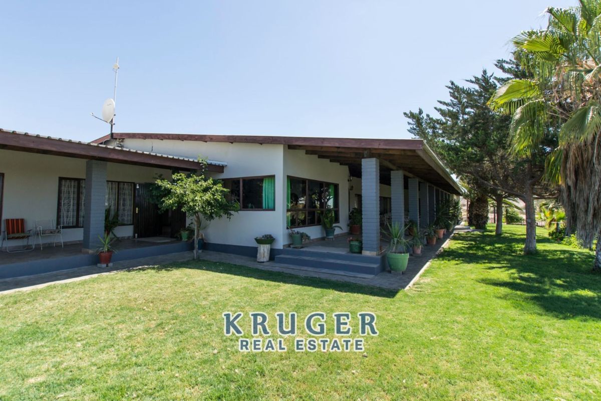 A spacious exterior view of the property featuring a large covered patio area with brick pillars, overlooking a well-maintained garden lawn.