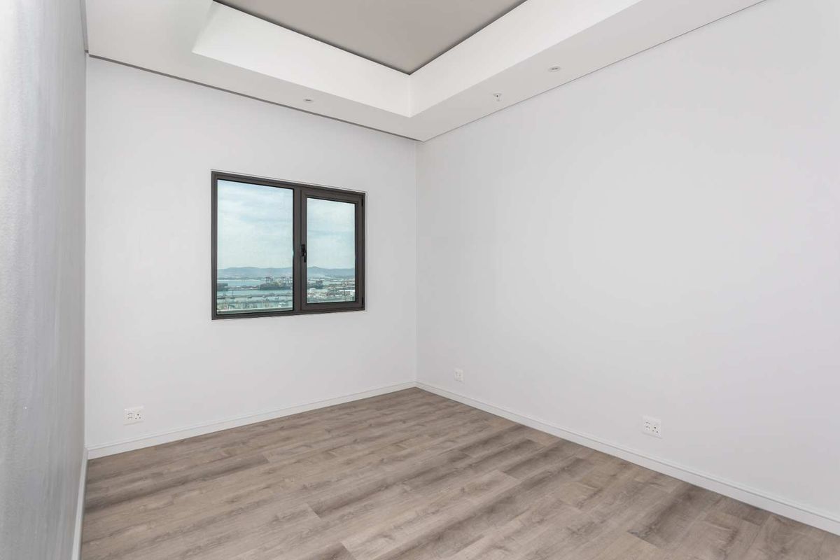 A bright, empty bedroom featuring modern wood-look flooring, a recessed ceiling detail, and a window offering expansive views.