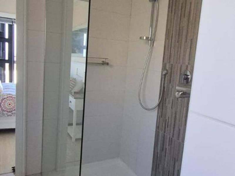 A modern bathroom featuring a walk-in shower with a glass screen, handheld shower head, and decorative tiled accent wall.