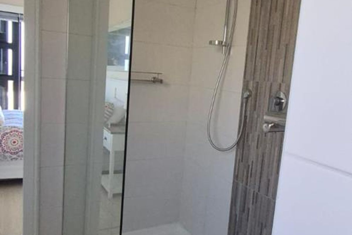 A modern bathroom featuring a walk-in shower with a glass screen, handheld shower head, and decorative tiled accent wall.