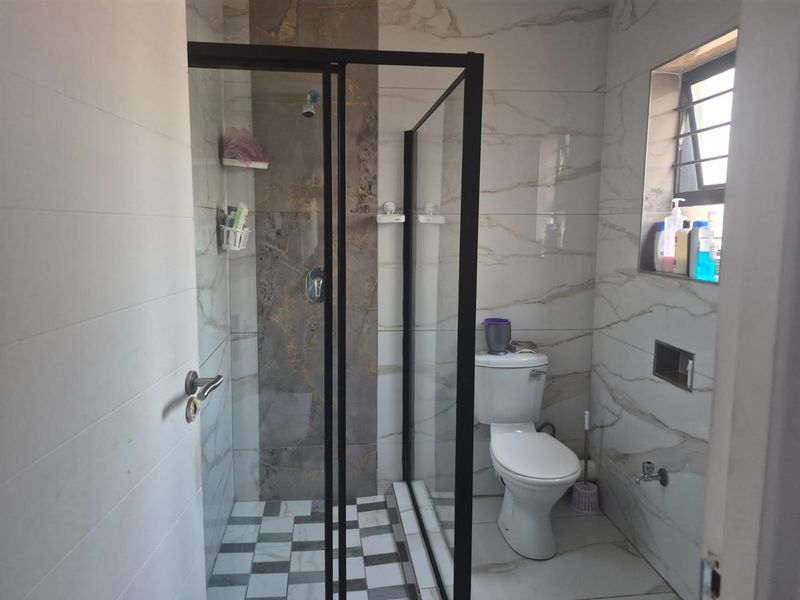 Modern bathroom featuring a walk-in shower with black-framed glass enclosure, marble-effect wall tiling, and a checkered floor pattern.