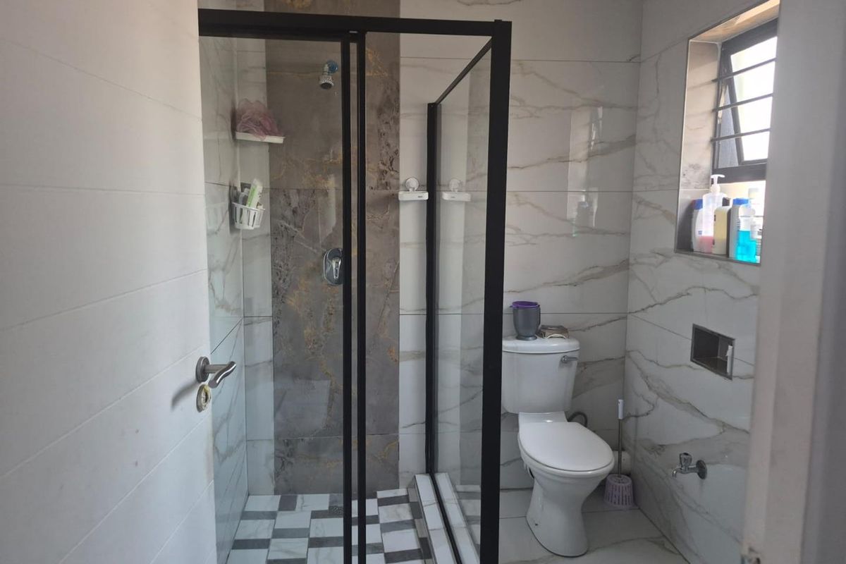 Modern bathroom featuring a walk-in shower with black-framed glass enclosure, marble-effect wall tiling, and a checkered floor pattern.