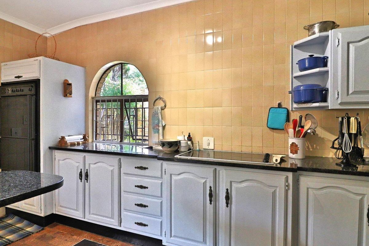 A functional kitchen featuring grey cabinetry, dark countertops, a built-in electric hob, and a distinctive arched window with security bars.