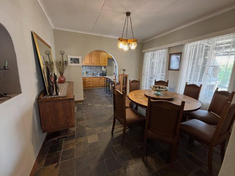 Open plan dining area featuring slate tile flooring and an arched transition into a traditional wooden kitchen with tiled backsplash.