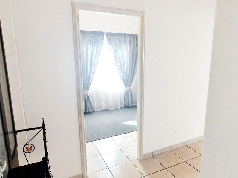 A bright, tiled hallway providing access to an adjacent room with carpeted flooring and window treatments.