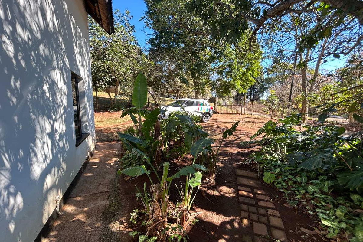 A view of the rear garden area featuring a paved walkway alongside the cottage exterior and a metal gate leading to the driveway.