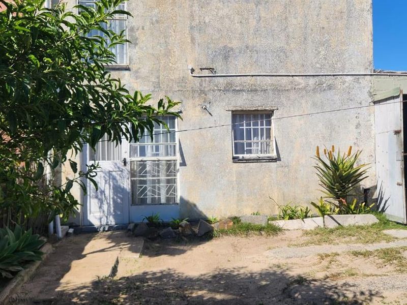 Rear exterior view of the property featuring a weathered facade, security bars on windows, and a small garden area.