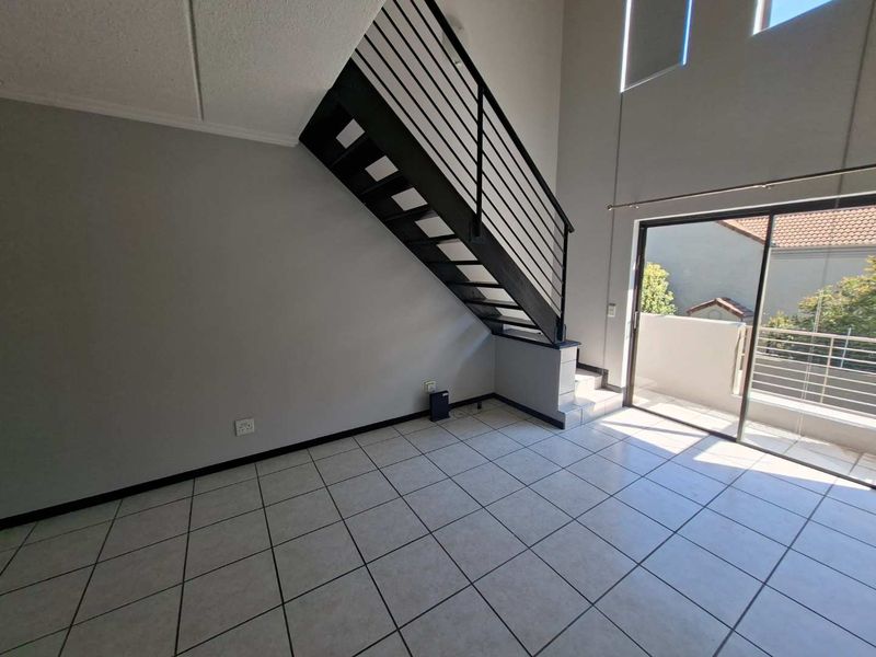 Spacious open-plan living area featuring tiled floors, a modern metal staircase, and large sliding doors leading to a private balcony.