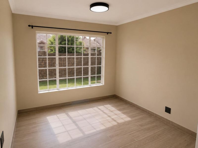 A bright, empty bedroom featuring neutral wall tones, modern tiled flooring, and a large grid-pattern window overlooking the garden.