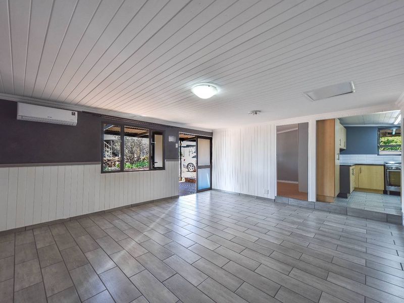 Spacious open-plan living area featuring tiled flooring, timber wall paneling, and an integrated kitchen space with modern finishes.