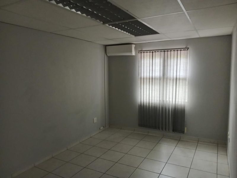 A vacant office space featuring ceramic floor tiles, a suspended ceiling with recessed lighting, and a wall-mounted air conditioning unit.