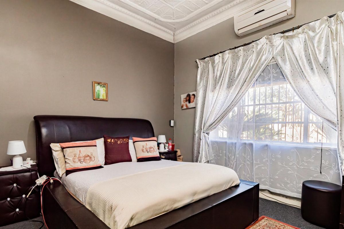 A comfortable bedroom featuring an ornate ceiling rose, decorative cornice, and a wall-mounted split-system air conditioner.