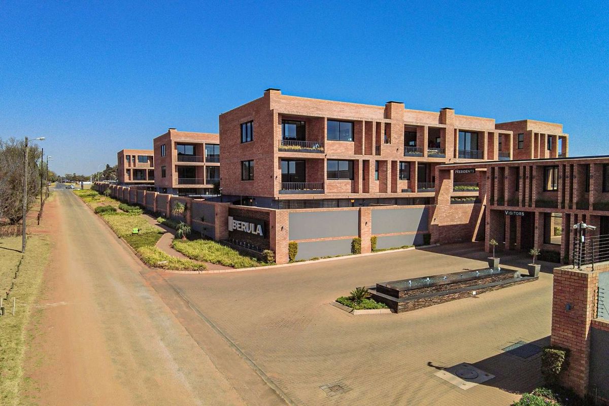 Aerial view of the Berula apartment complex, showcasing modern brick architecture, paved entrance, water feature, and secure perimeter walling.