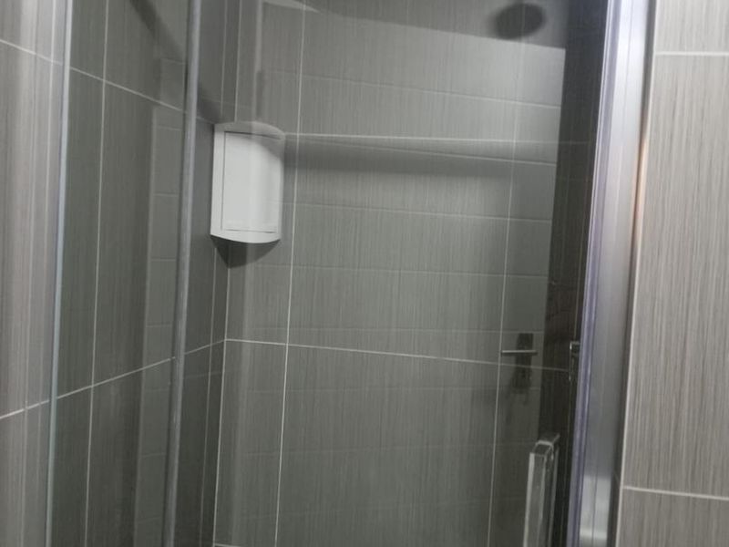 A modern bathroom shower enclosure featuring grey tiled walls, a glass door, and a built-in corner soap dish.