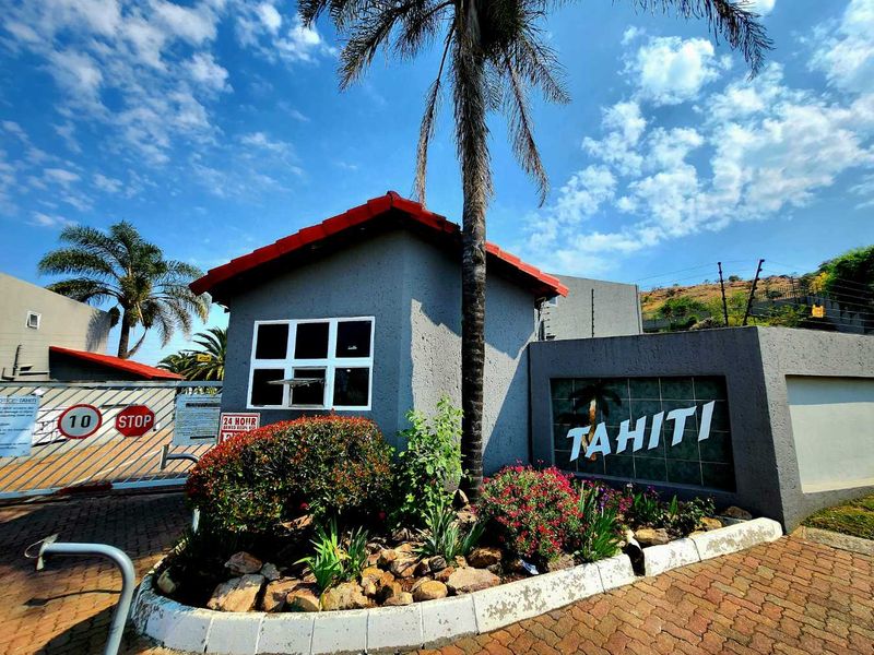 Front entrance view of the Tahiti townhouse complex featuring a security gate, guard booth, and paved driveway access.