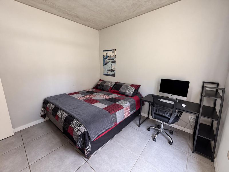 A functional bedroom featuring tiled flooring and an exposed concrete ceiling, providing a neutral base for personalization.