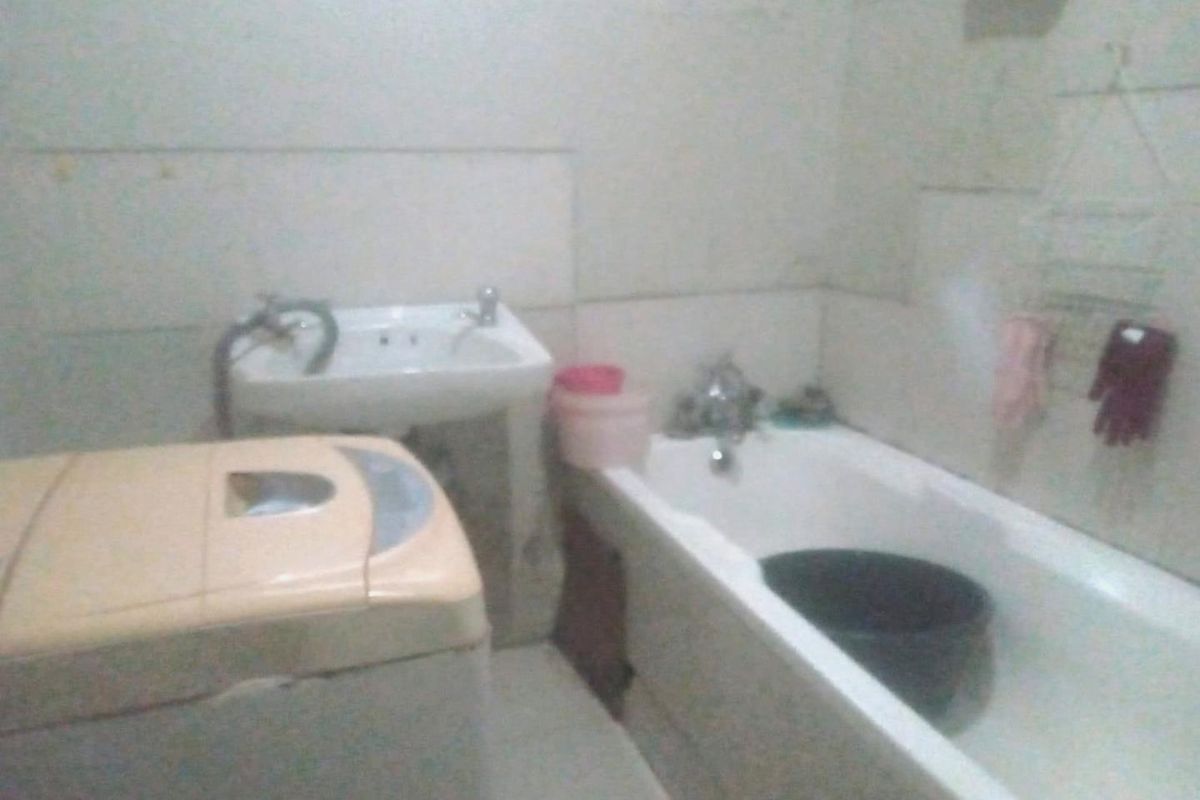 A compact bathroom featuring a standard bathtub and a wall-mounted basin, requiring cosmetic updates to improve the overall aesthetic and functionality.
