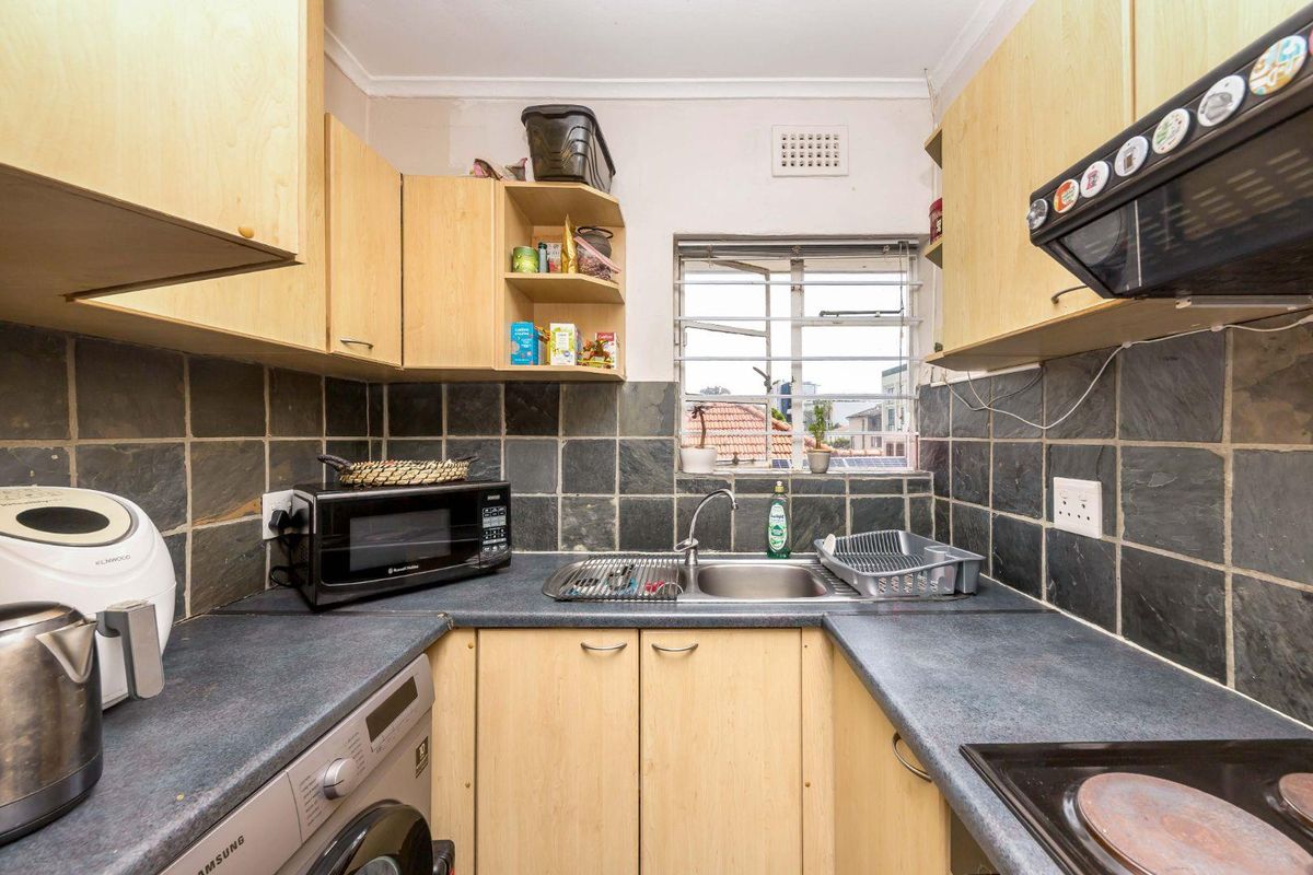 Compact kitchen featuring laminate cabinetry, slate tile backsplash, integrated hob, and extractor fan, offering a functional layout with potential for modern updates.