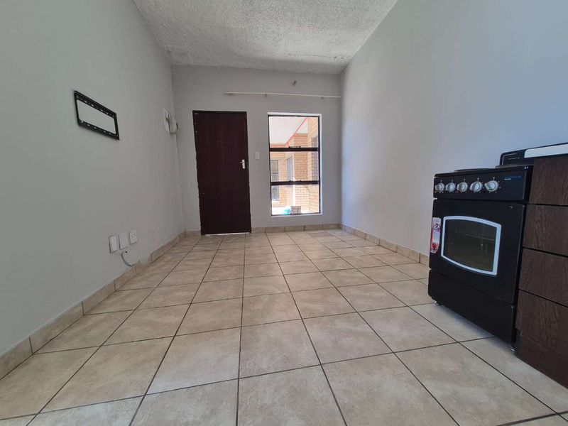 A compact, empty kitchen area featuring tiled flooring, a built-in oven, and a textured ceiling, offering a blank canvas for renovation.