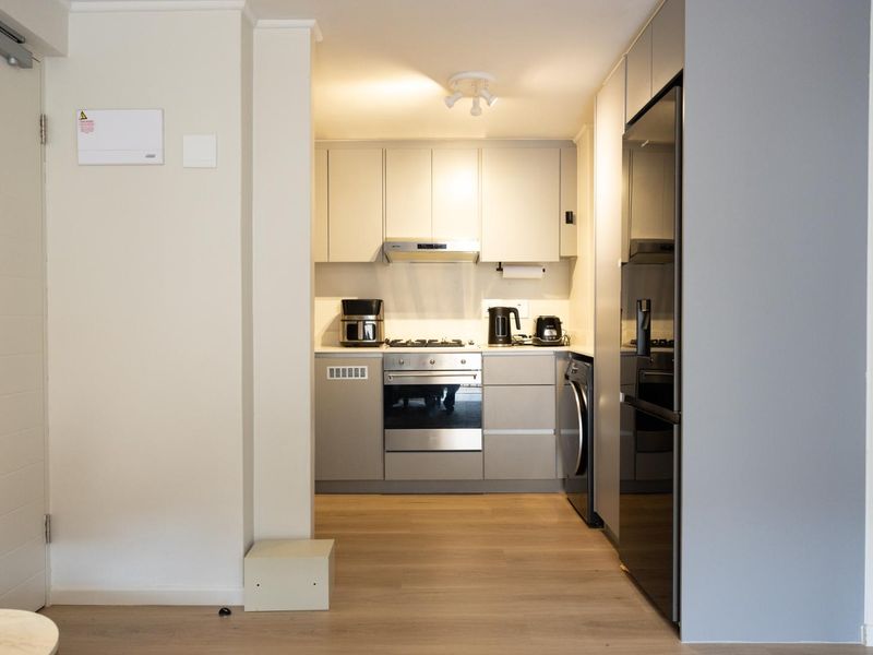 A compact, modern kitchen featuring neutral cabinetry, integrated appliances, and light wood-look flooring, offering a clean and functional workspace.