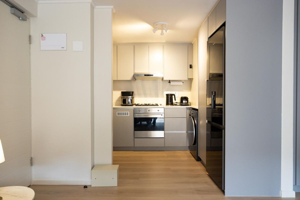 A compact, modern kitchen featuring neutral cabinetry, integrated appliances, and light wood-look flooring, offering a clean and functional workspace.
