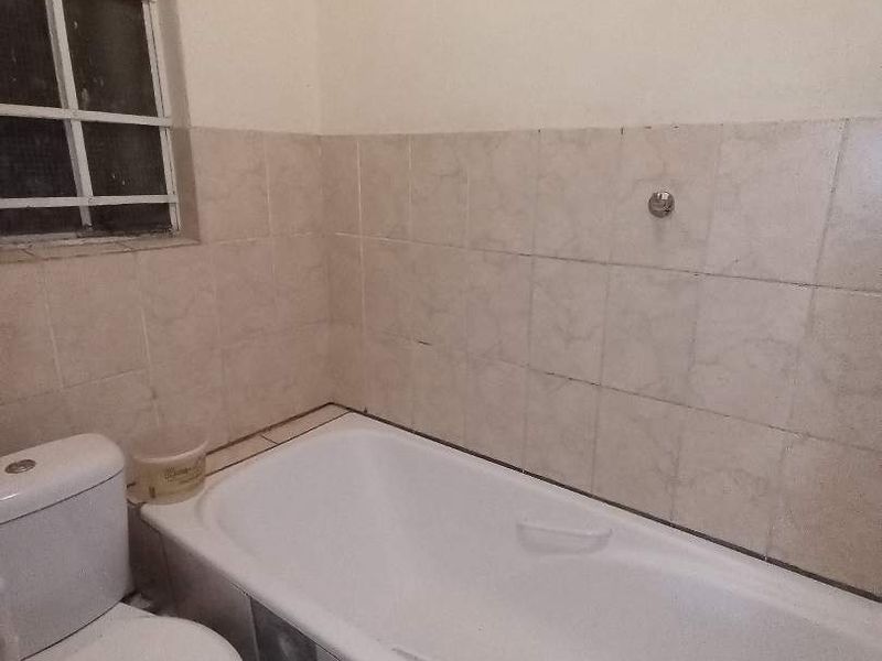 A functional bathroom featuring a standard bathtub, toilet, and neutral wall tiling, requiring minor cosmetic updates to improve its overall condition.