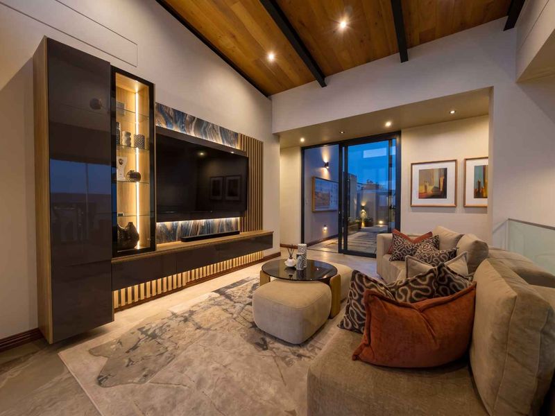 Modern living room featuring a high timber-clad vaulted ceiling, custom built-in media cabinetry with integrated lighting, and seamless access to an outdoor area.