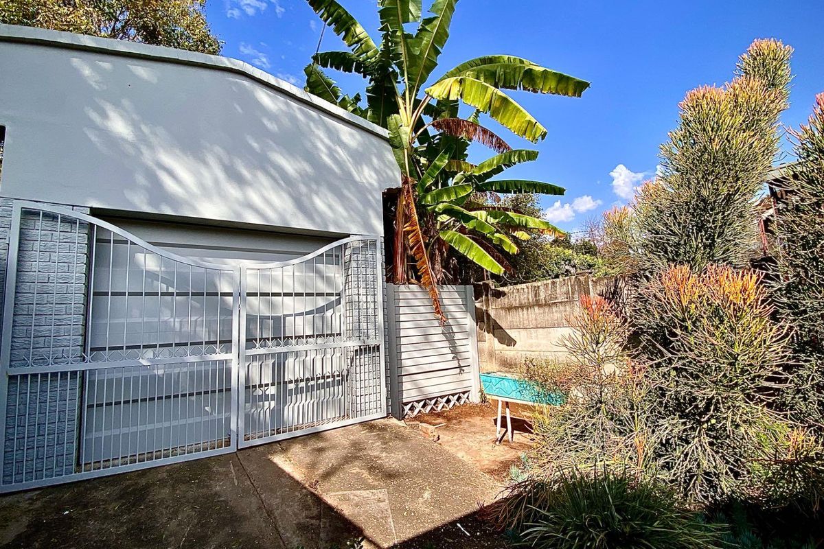 A view of the property's exterior rear area featuring a secure metal gate, concrete paving, and established garden landscaping.