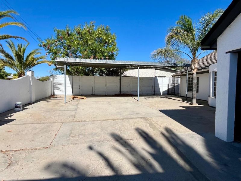 A spacious rear exterior area featuring a concrete driveway, a metal carport structure, and secure perimeter walling.