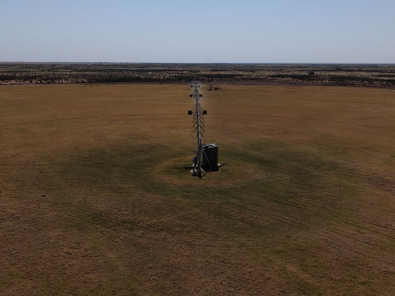 Aerial view of a large agricultural field featuring a center pivot irrigation system and a water storage tank.