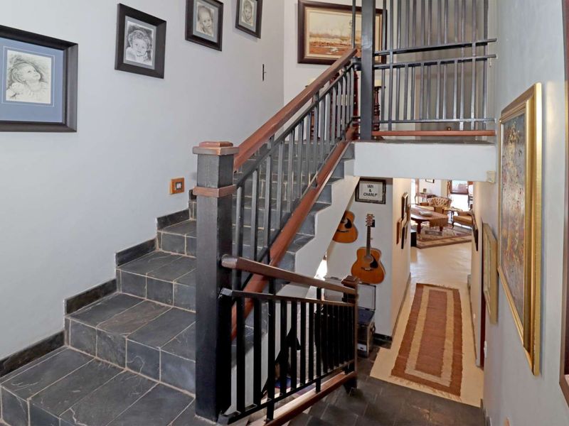 A well-maintained interior hallway featuring a stone staircase with a metal balustrade and wooden handrail, leading to an open-plan living area.